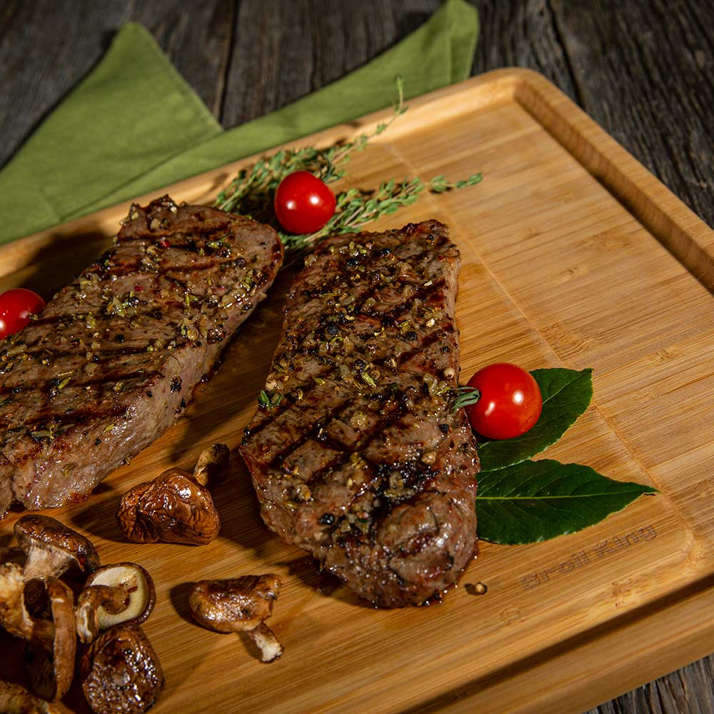 Bamboo cutting board with grilled meat, mushrooms, cherry tomatoes, and herbs