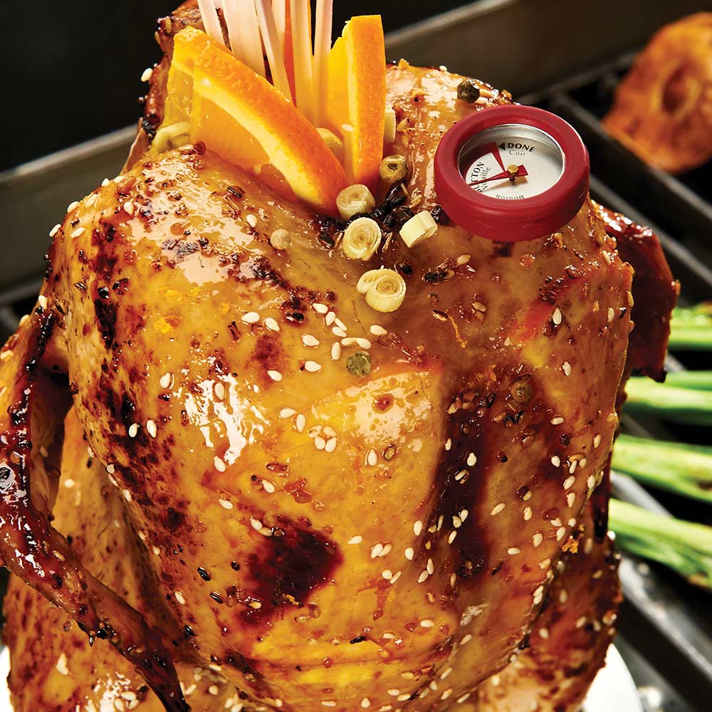 Roasted chicken on stand with pineapple wedges, green herbs, and red thermometer