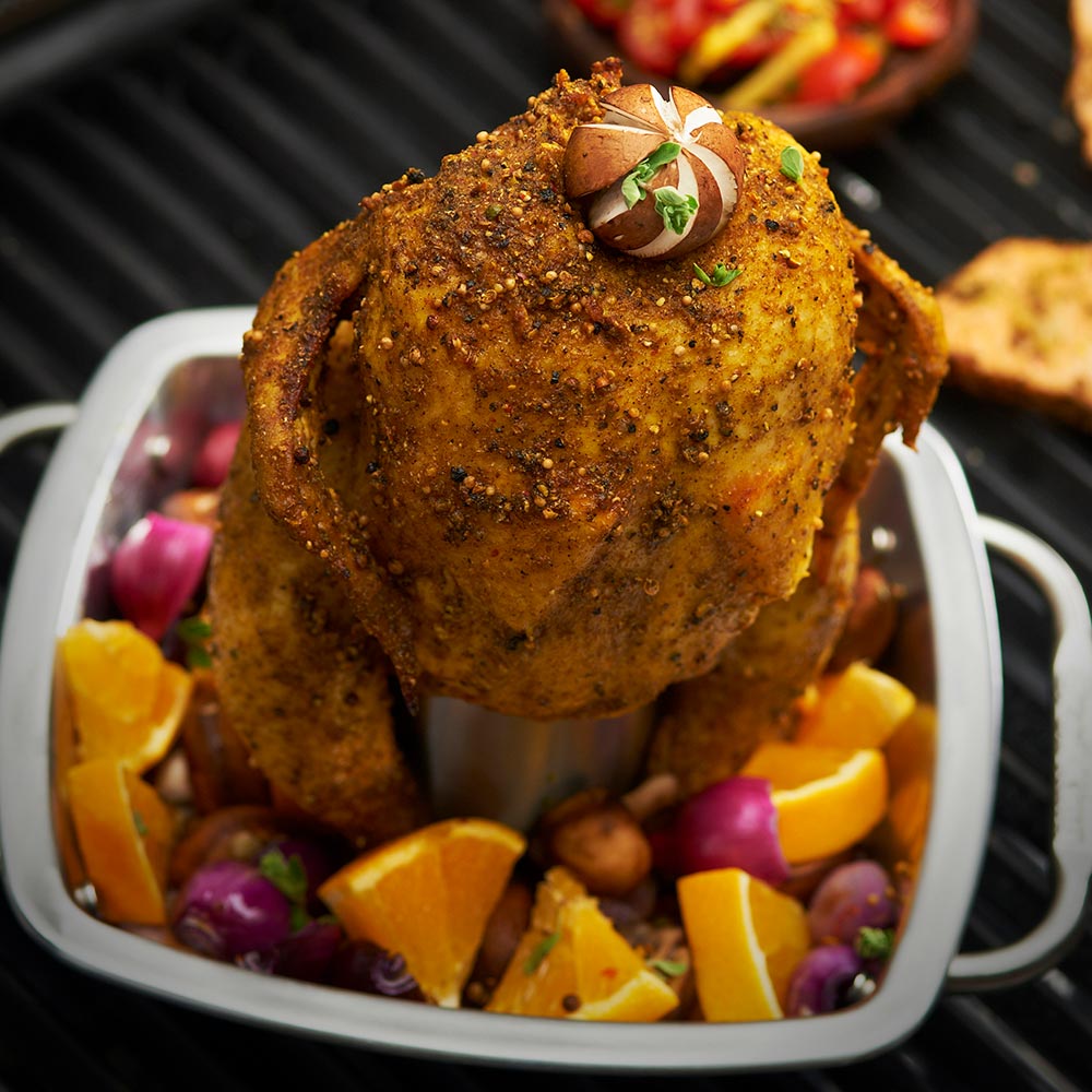 Chicken roaster pan with roasted chicken on a center post and assorted vegetables