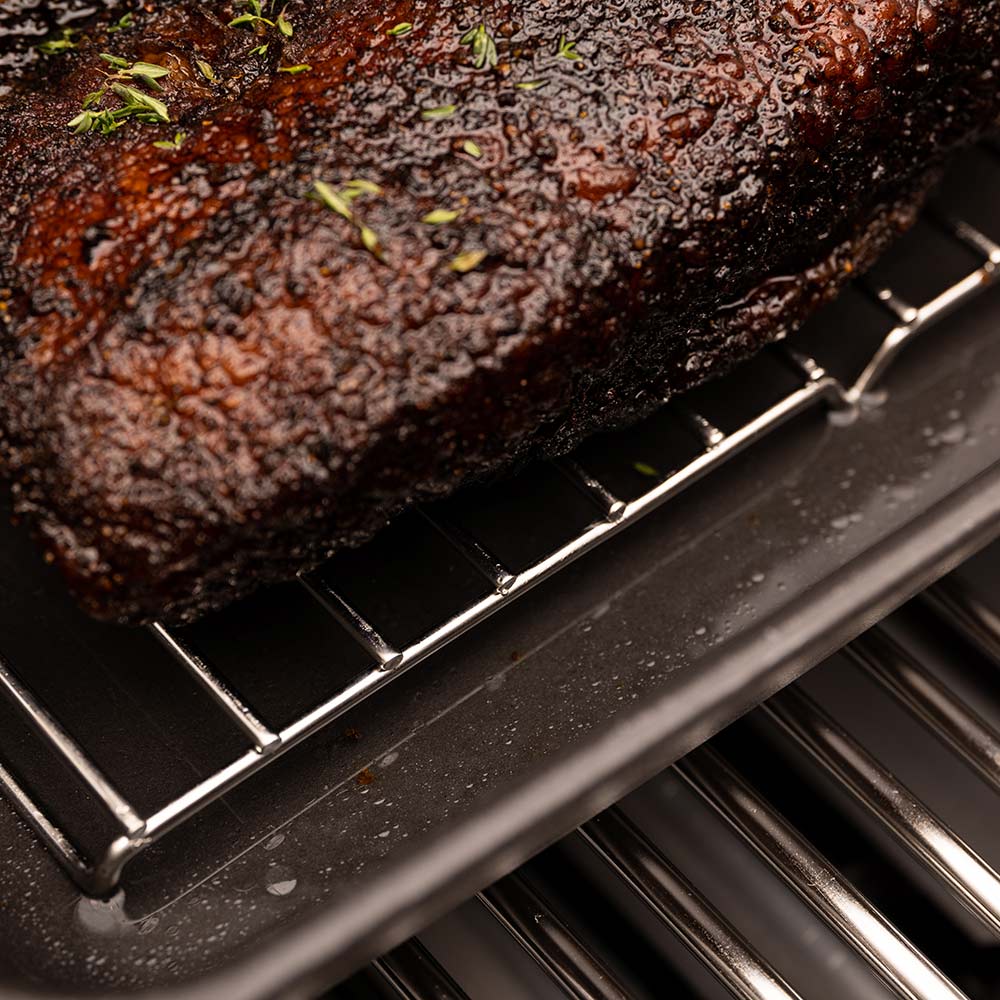 Close-up of seasoned roast on cast iron roaster rack with herbs and drips
