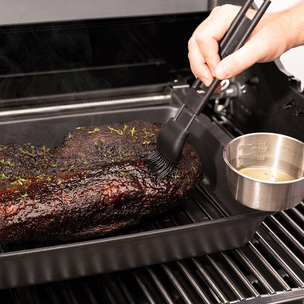Cast iron multi roaster with roast brushed with sauce, sauce cup beside tray