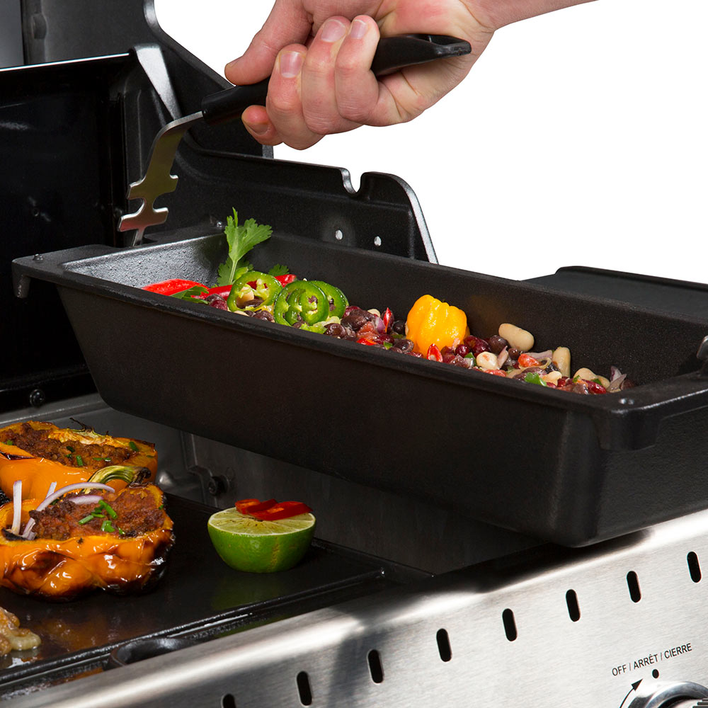 Black cast iron wok insert being placed on a grill with food inside