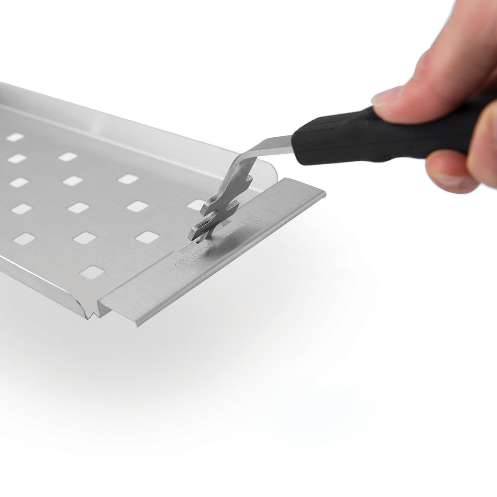 Narrow stainless steel grill topper tray being lifted by a black-handled tool