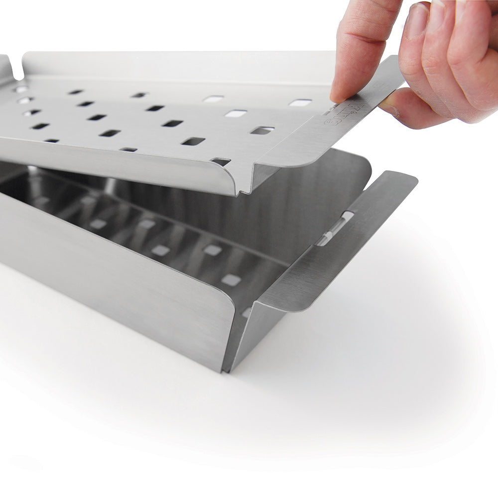 Narrow stainless steel grill topper tray on grill with hands adjusting the side rim
