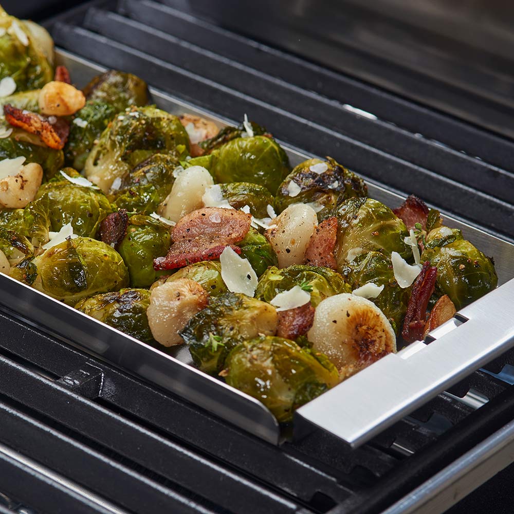Narrow stainless steel grill topper tray holding roasted vegetables on grill grates