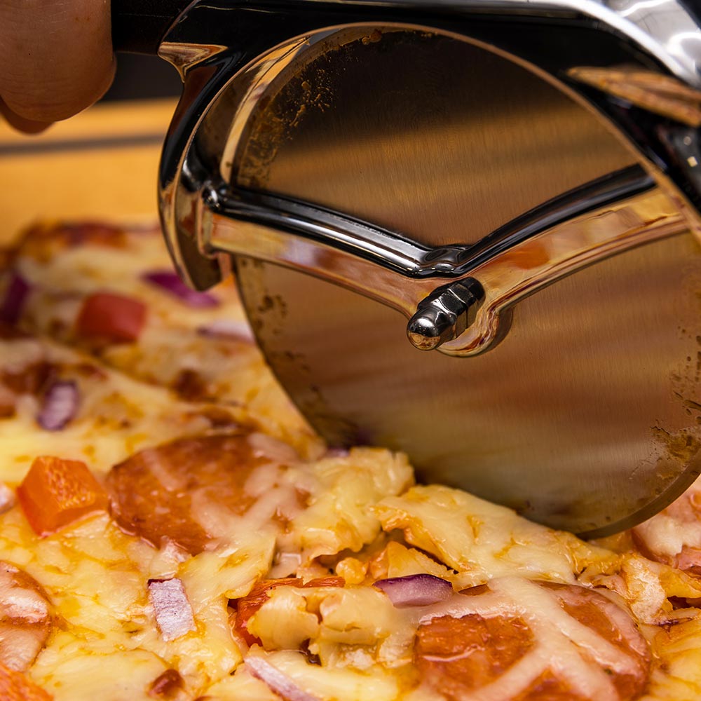 Close-up of pizza cutter wheel on cheesy pizza