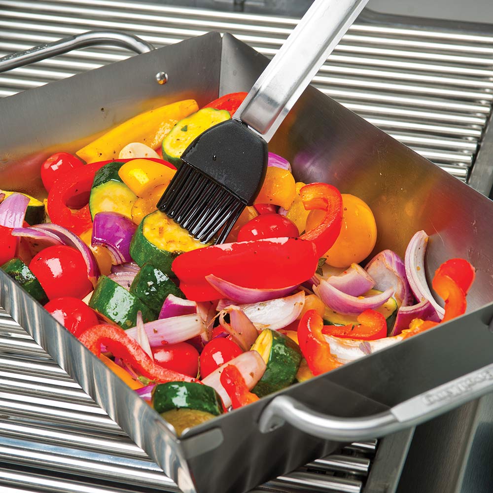Stainless steel grill wok topper with side handles, filled with sliced vegetables on grill.