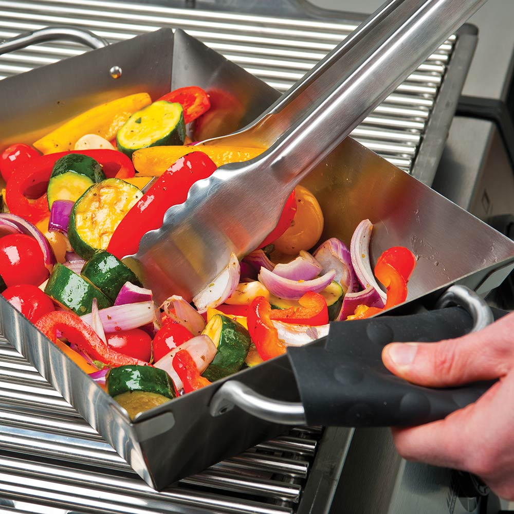Stainless steel grill wok topper with side handles and spatula, vegetables cooking.