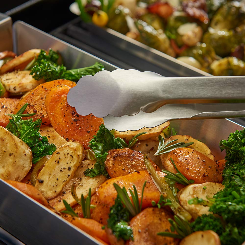 Roasted vegetables in stainless steel wok grill topper with tongs and spatula