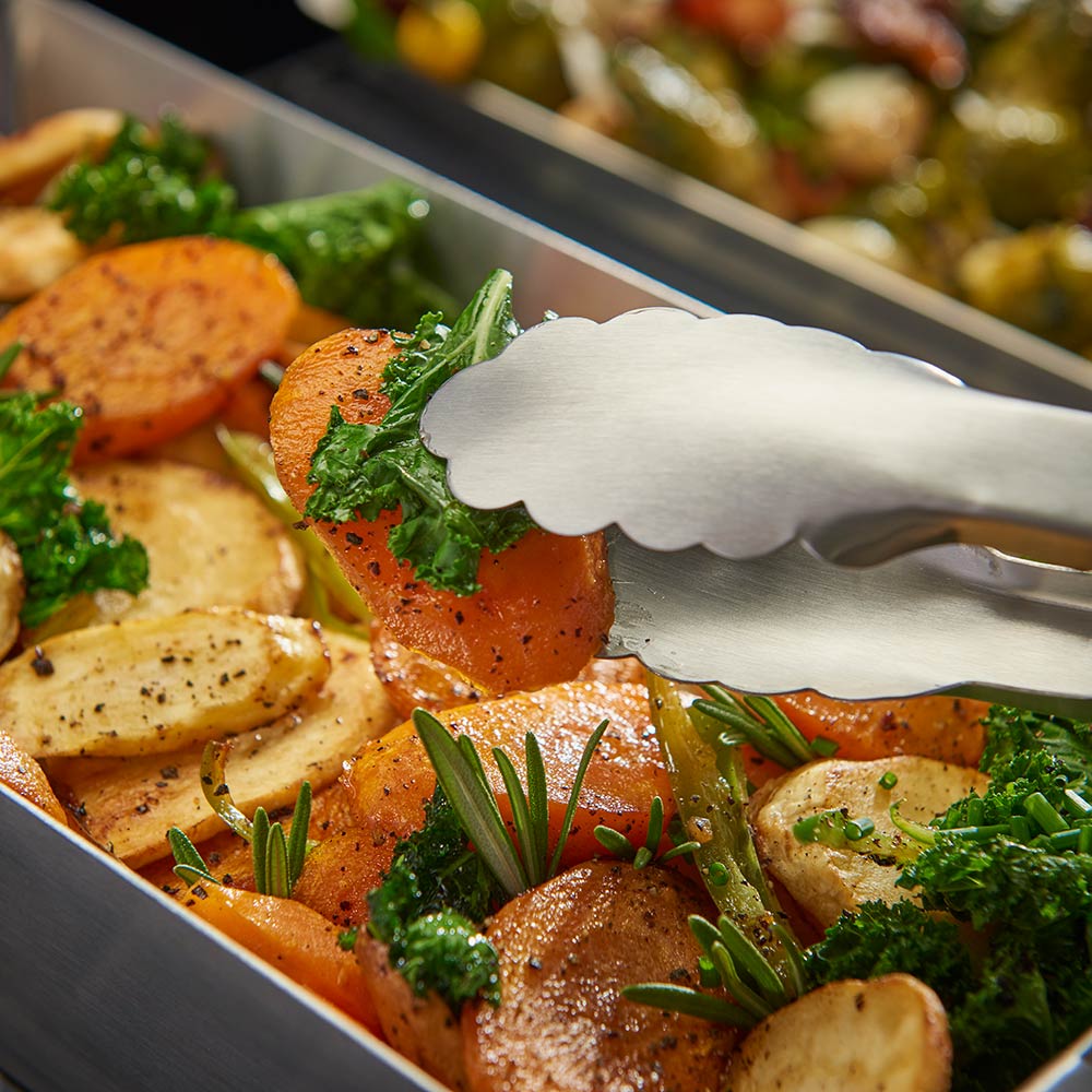 Roasted vegetables in stainless steel wok grill topper with herb garnish, spatula