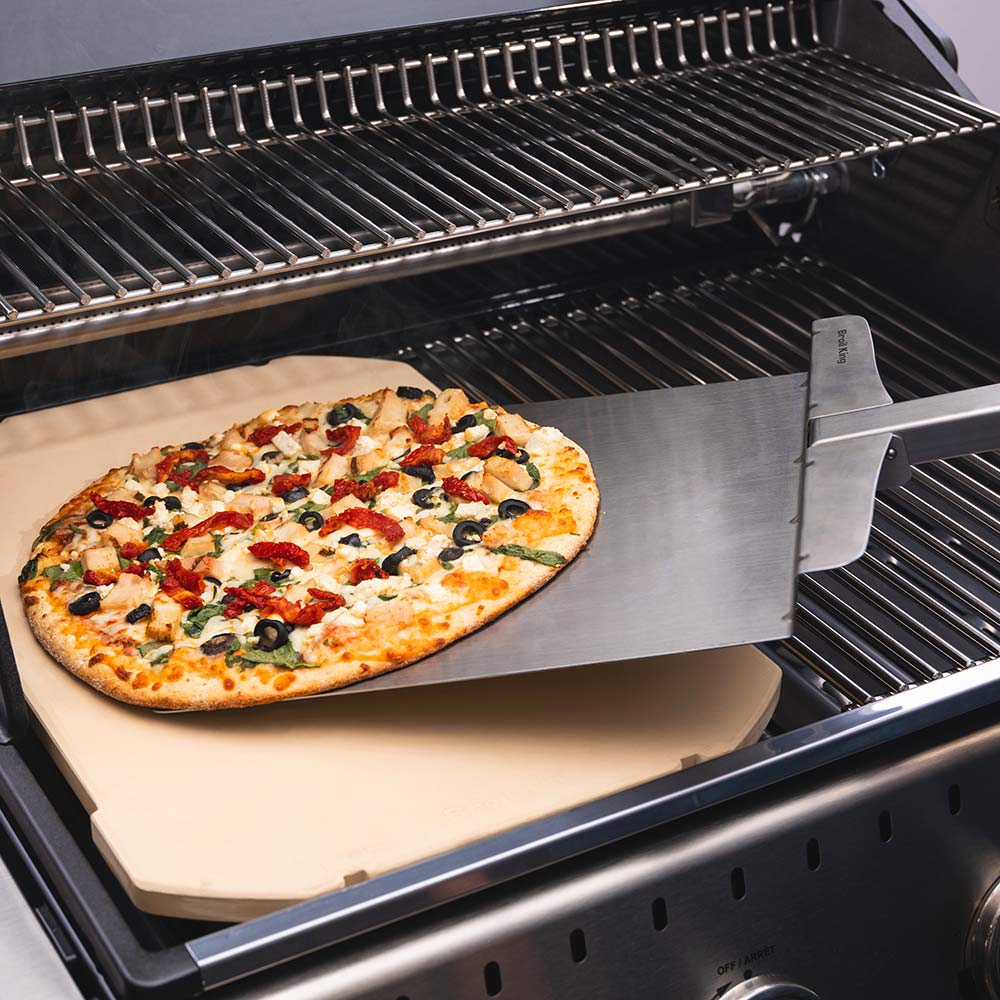 Rectangular pizza stone holding pizza on a grill, beige ceramic surface