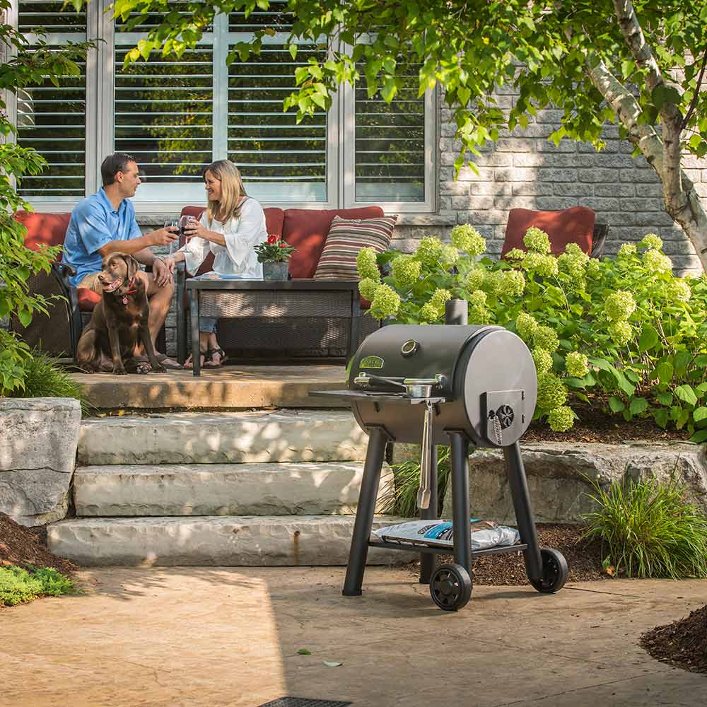 Charcoal smoker grill on wheels with lid open and food grilling inside outdoors