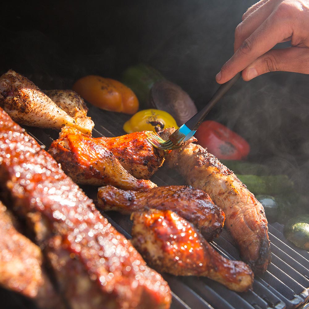 Charcoal smoker grill with sausages and peppers on dark grates, smoke and grilling juices