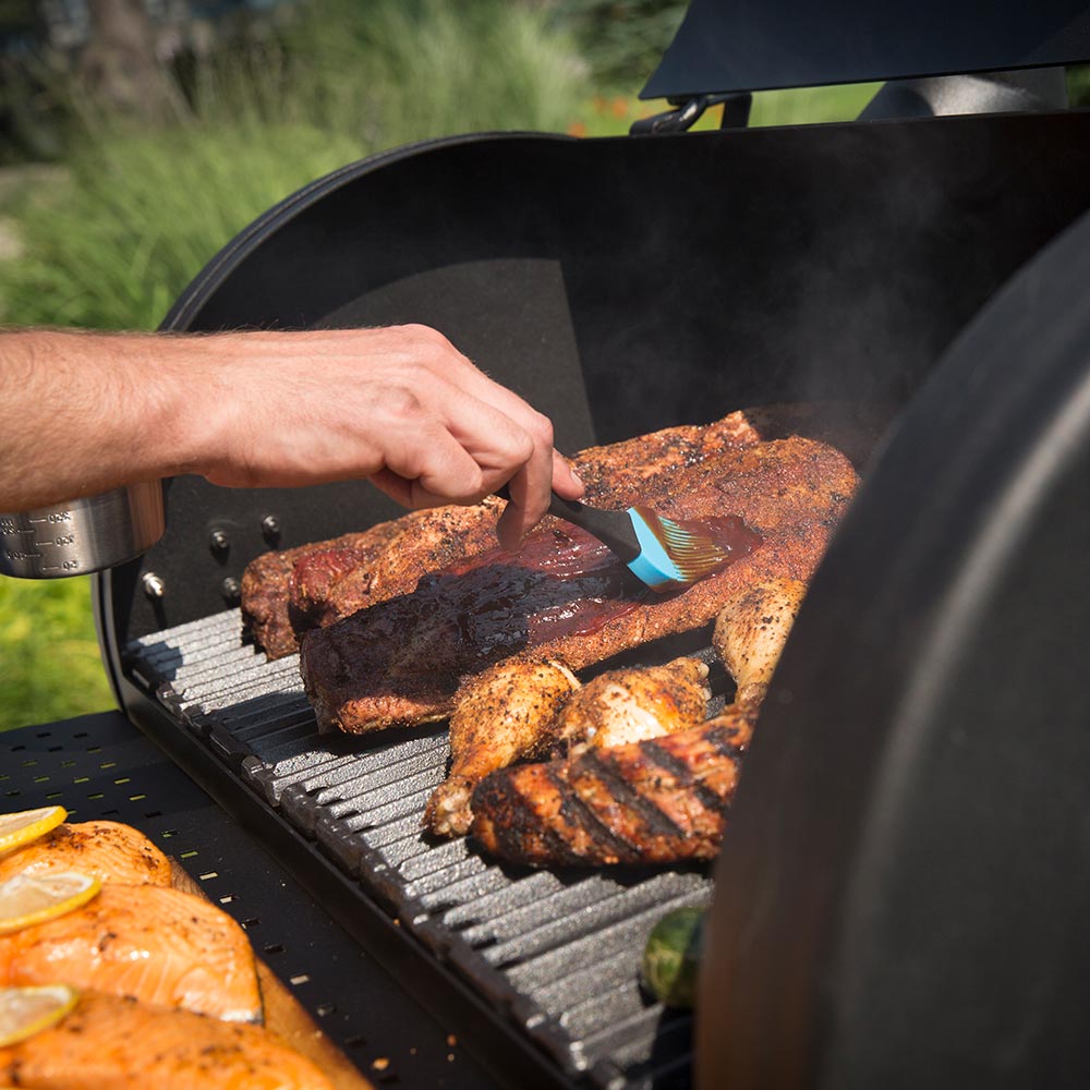 Person adding meat to a charcoal smoker grill with hood open and cooking grates visible
