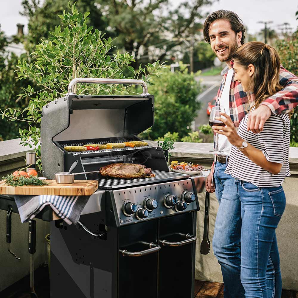 Gas grill with lid open and cooking grates, featuring a roast on the burners