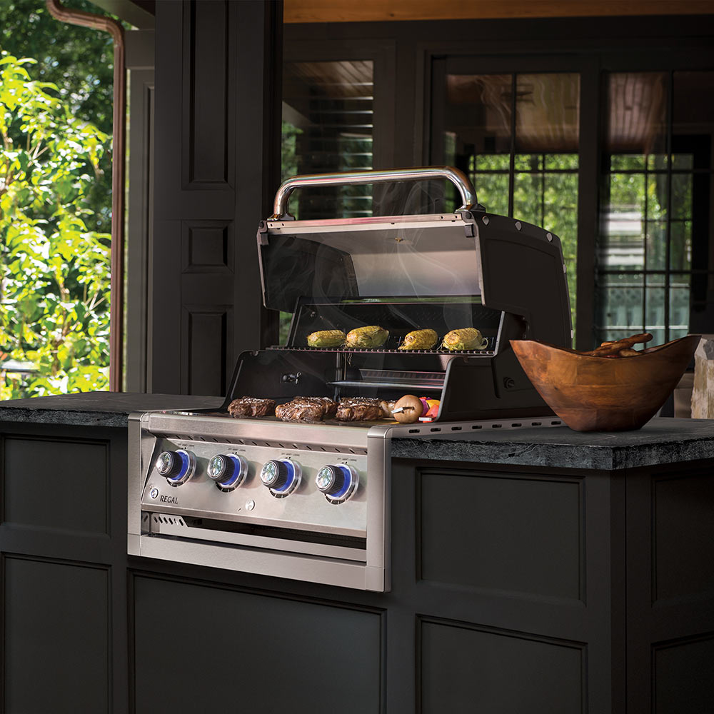 Stainless steel 4-burner built-in gas grill head with lid open, cooking grate and food