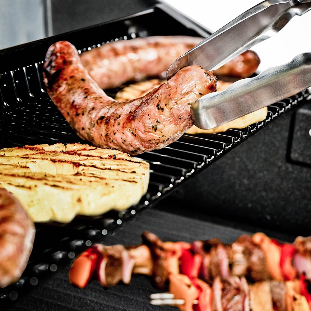 Grilled chicken on black grill grates with metal tongs