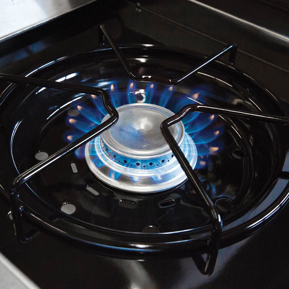 Gas grill burner with blue flames beneath round cooking grate