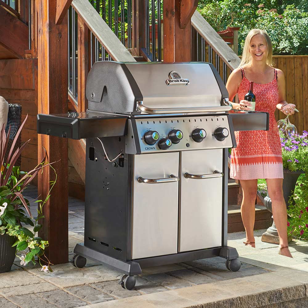 Stainless steel 4-burner gas grill with open lid and two cabinet doors, outdoor patio view