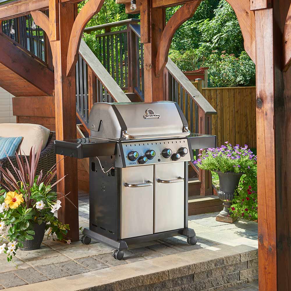Stainless steel 4-burner gas grill with cooking area open, two cabinet doors, patio view