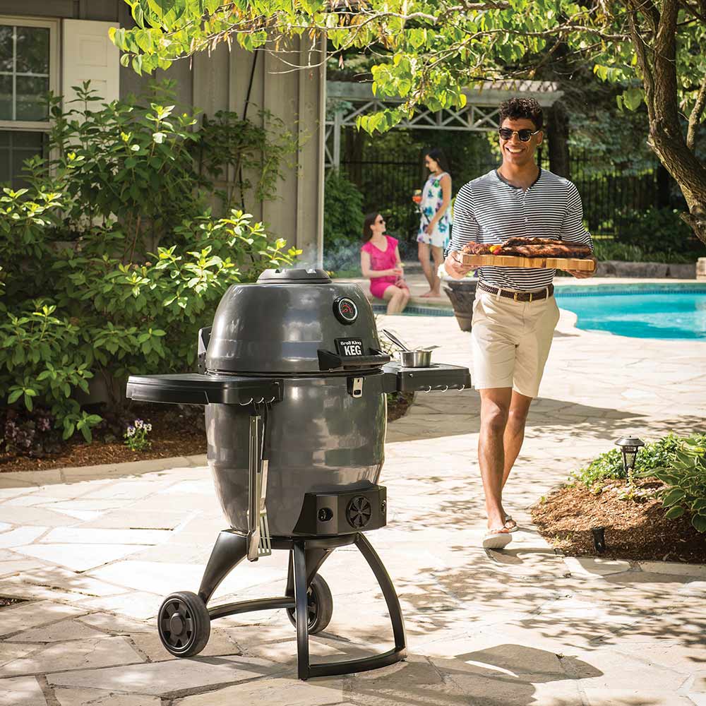 Charcoal smoker on wheeled stand beside pool patio, with domed lid, black