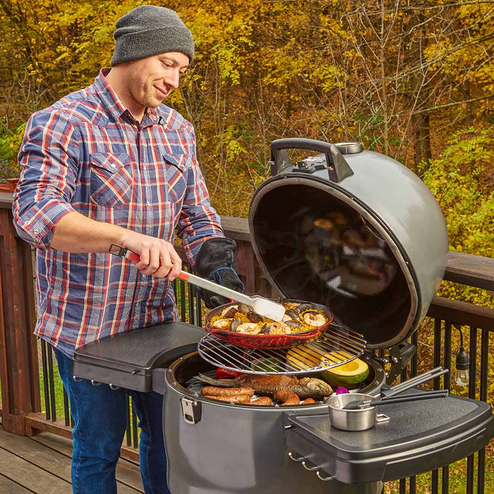 Outdoor charcoal smoker with open lid on deck, with food cooking on grate, dark