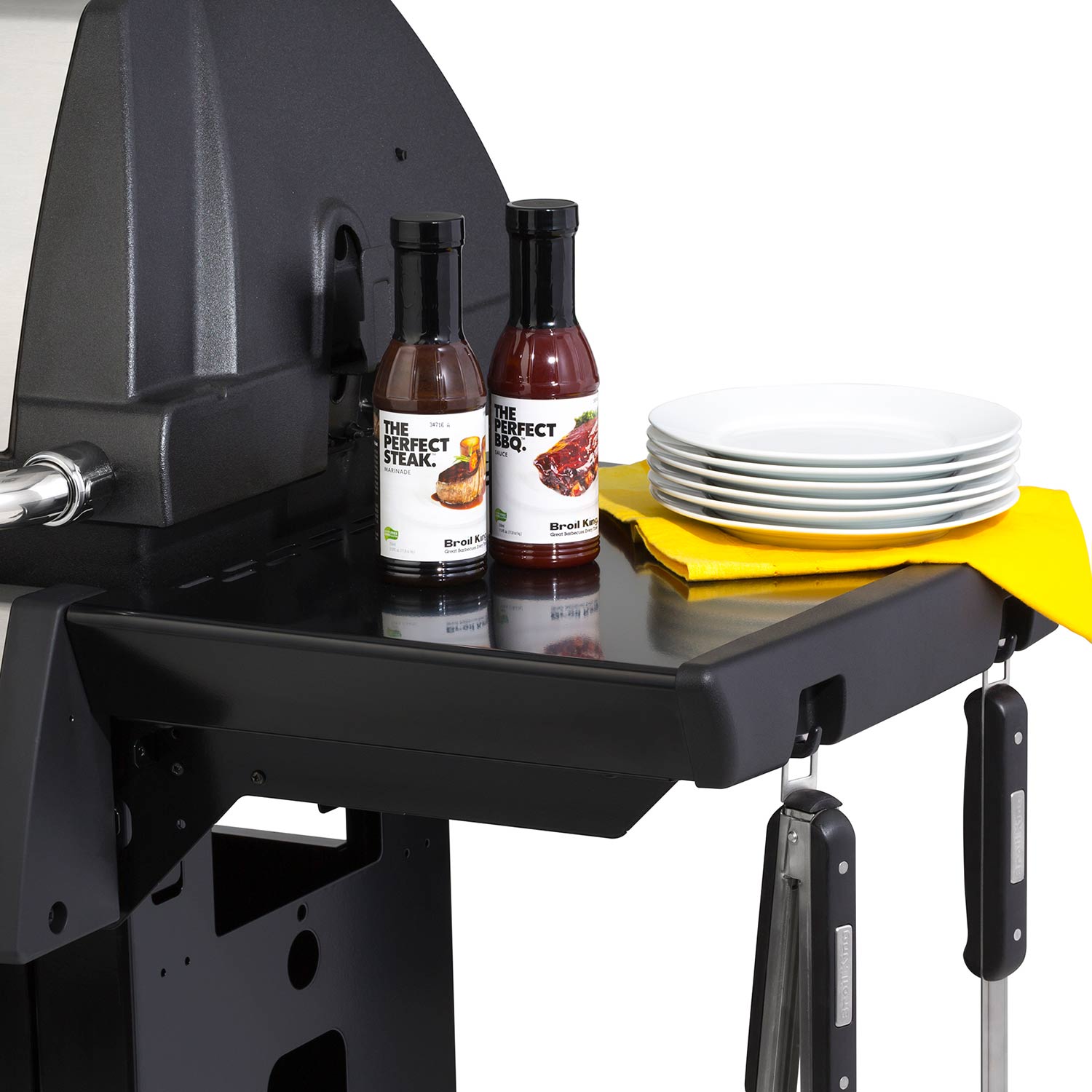 Grill side shelf with condiment bottles and stacked plates next to the grill body