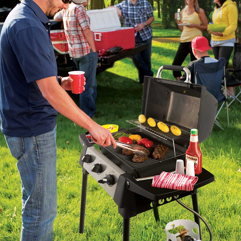 Portable propane grill outdoors with food on the cooking grate