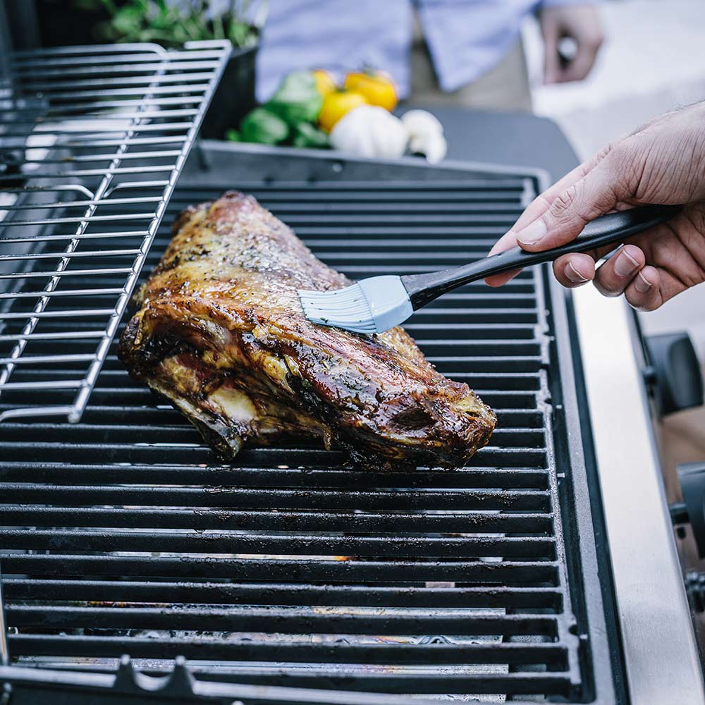 Portable propane grill grate with roasted meat being turned with tongs