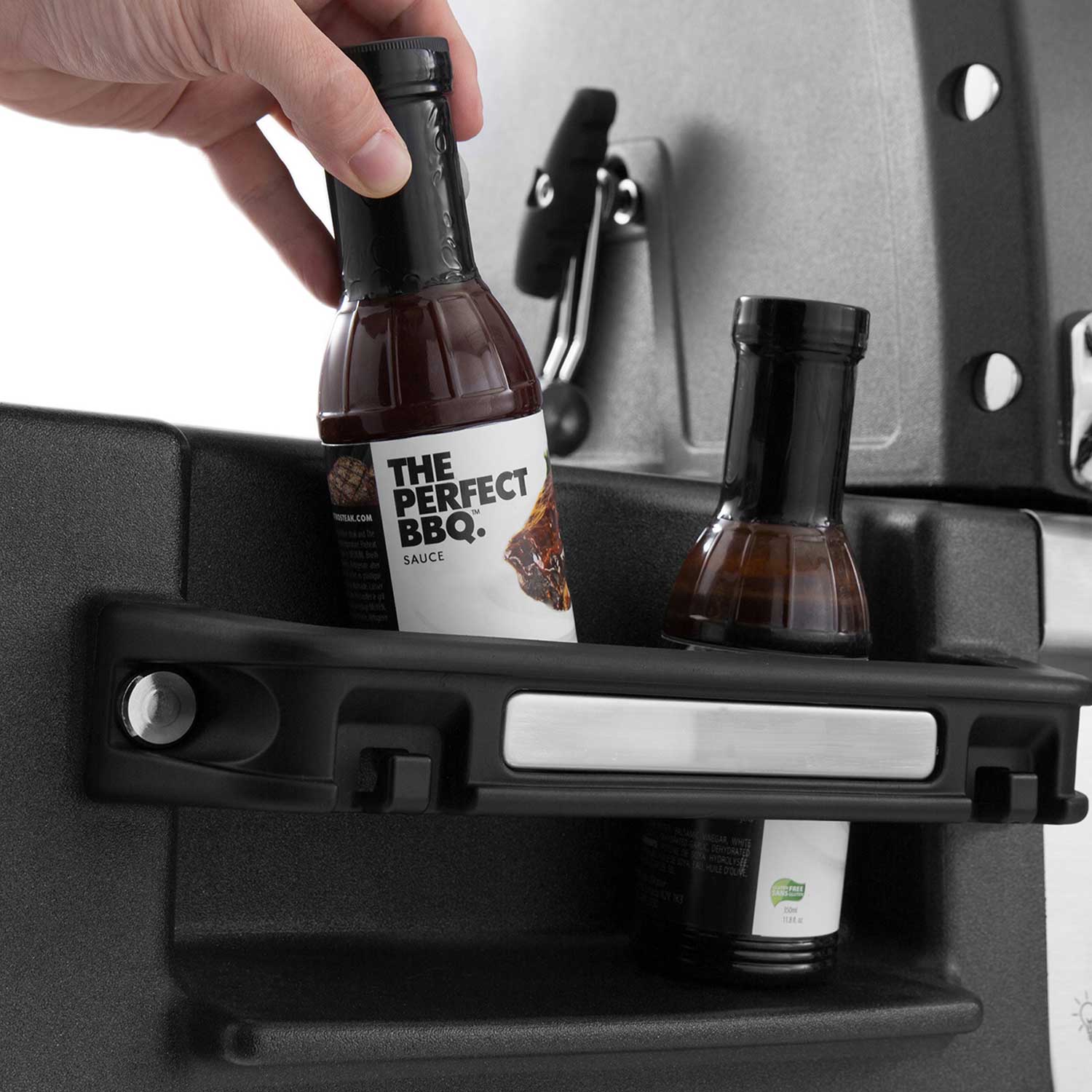 Gas grill with side shelf holding BBQ sauce bottles and condiment tools