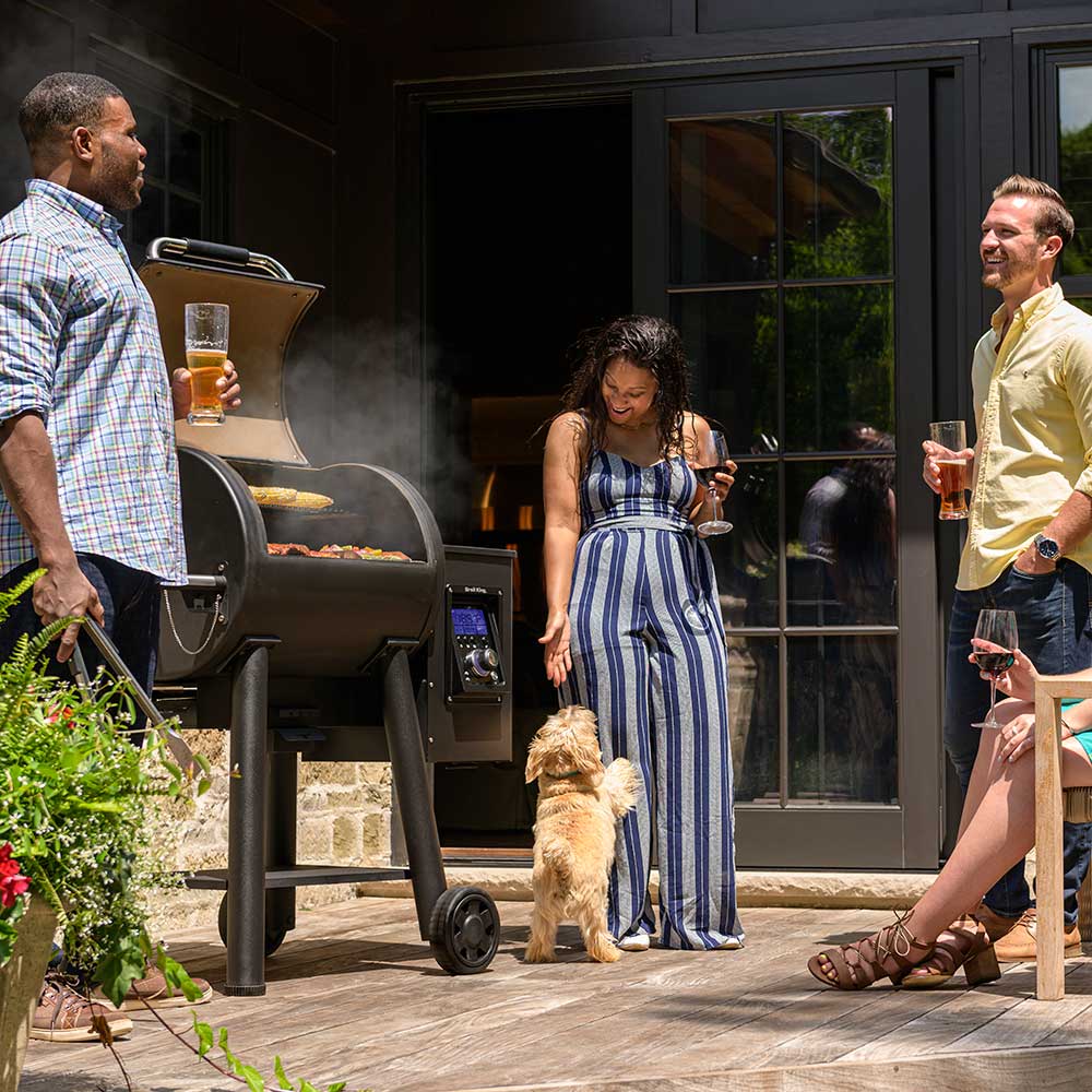 Pellet smoker and grill emitting smoke with closed lid near a home doorway