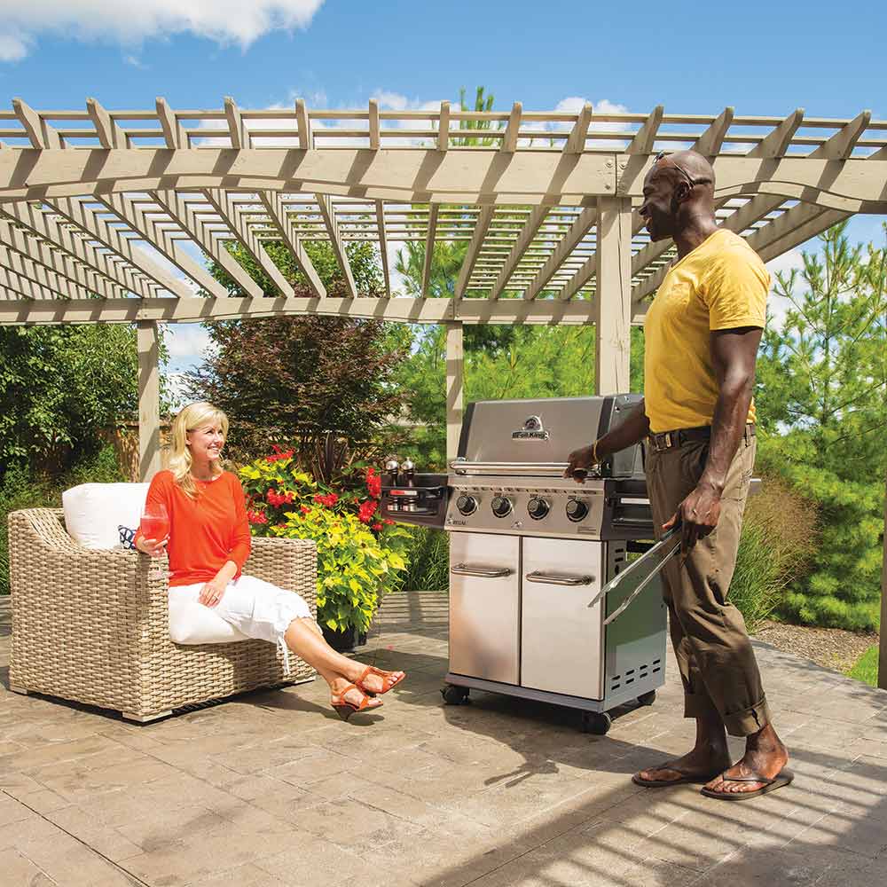 Freestanding stainless steel gas grill with open lid, outdoor patio setup