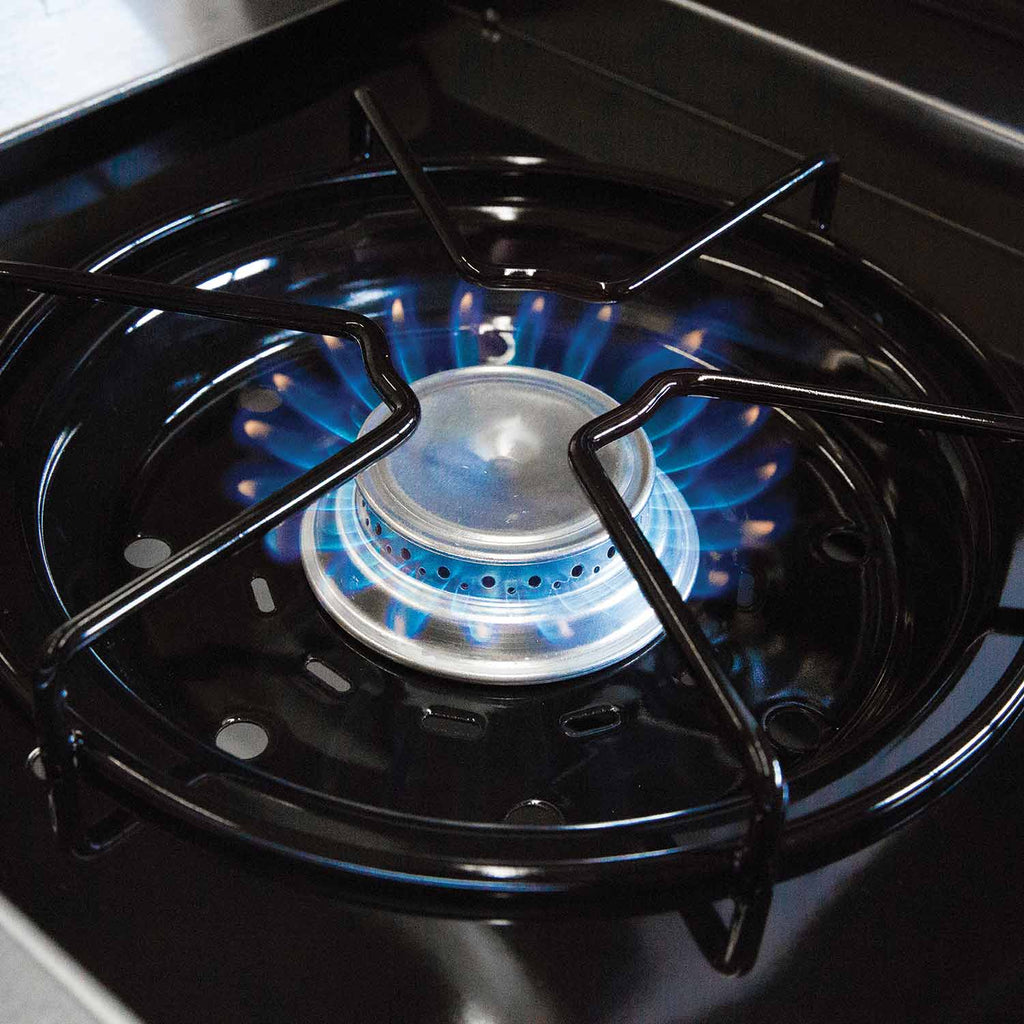 Gas grill burner basin with active blue flame and metal flame ring