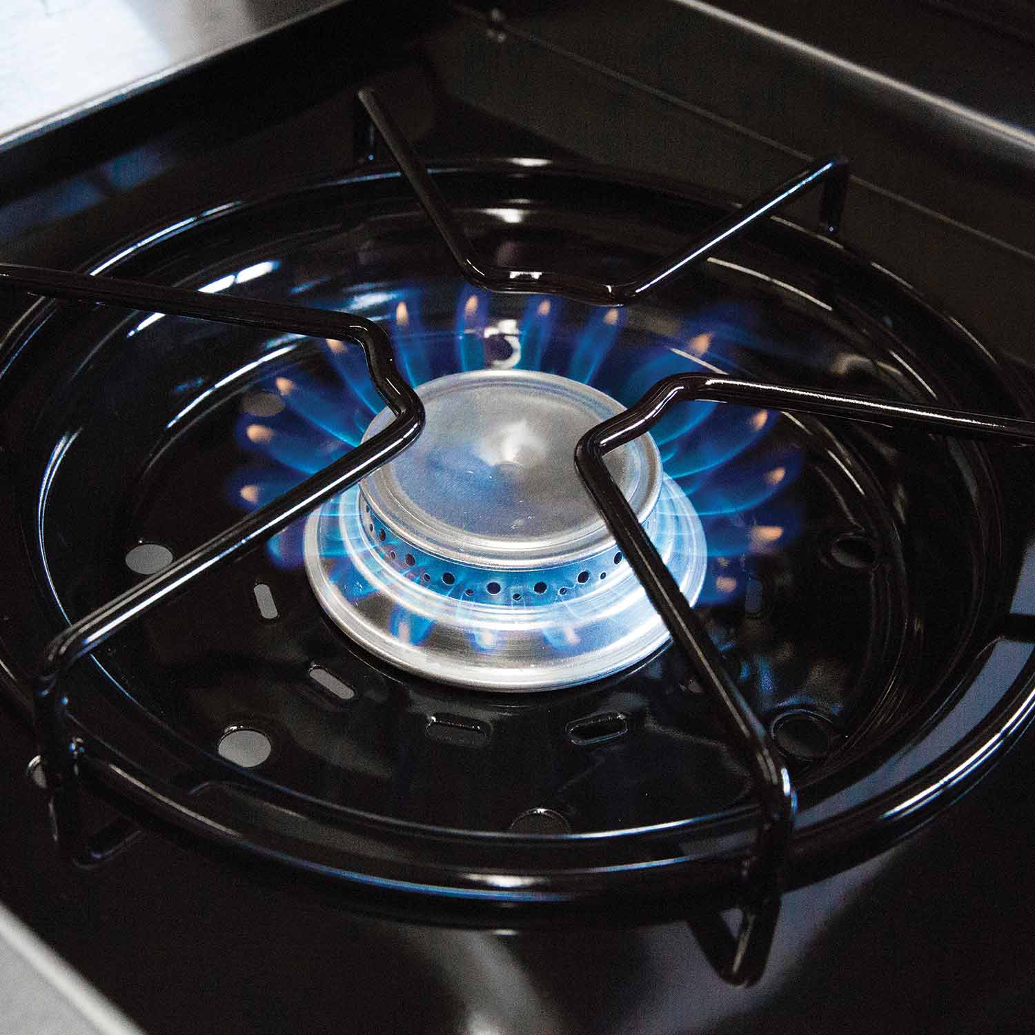 Gas grill burner basin with active blue flame and metal flame ring