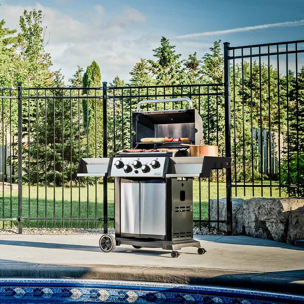 Gas grill on 2-wheel cart outdoors with lid open and control knobs visible
