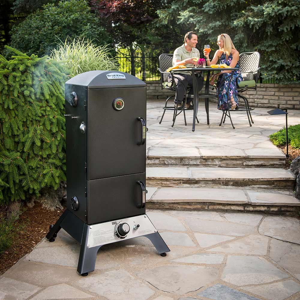 Vertical gas smoker with closed doors and front control panel on legs outdoors