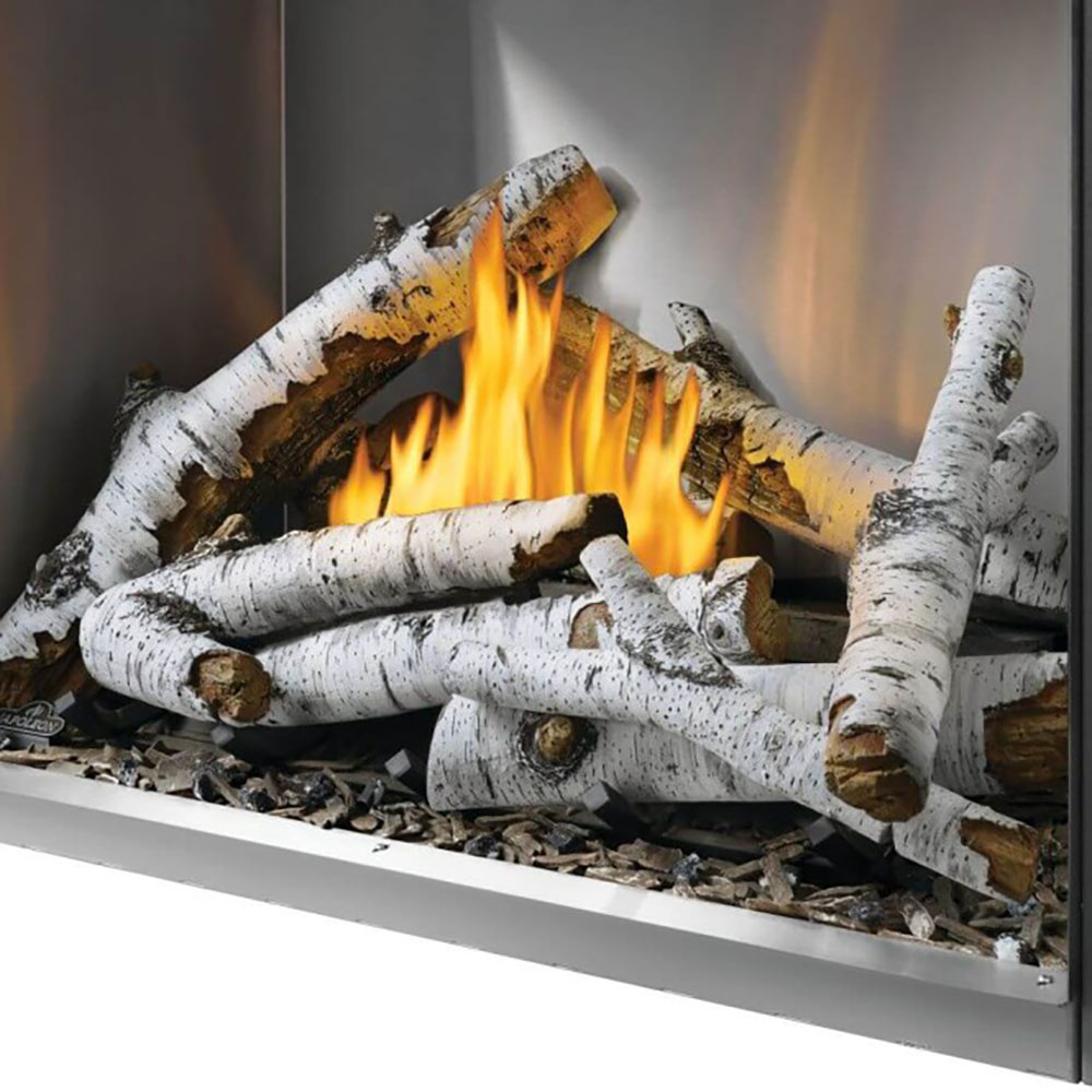 Outdoor gas fireplace log kit with white birch-style logs burning in an outdoor firebox
