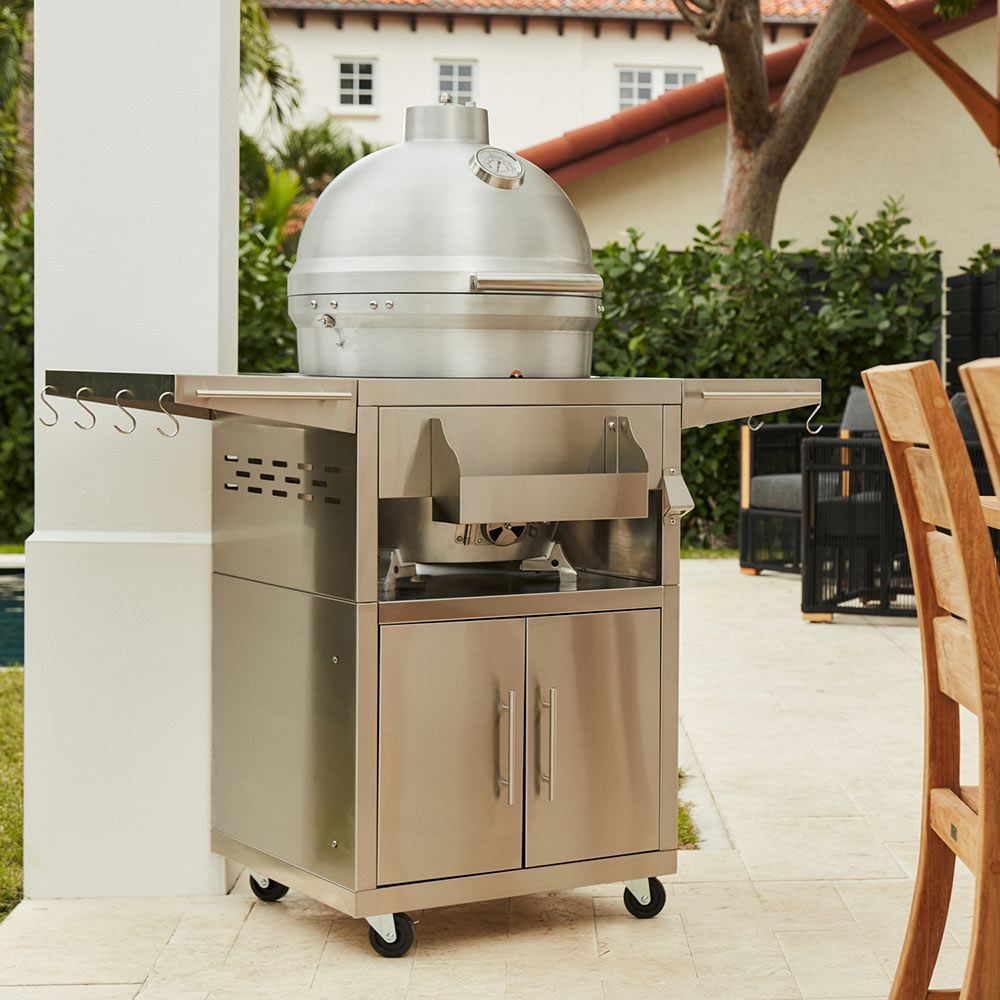 Aluminum kamado grill on outdoor cart with lid open and prep cabinet doors