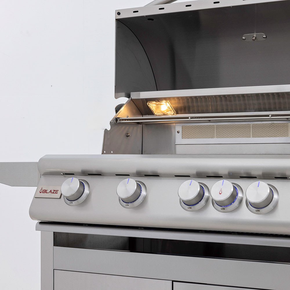 Gas grill with lid open and glowing burner flame inside the cooking chamber