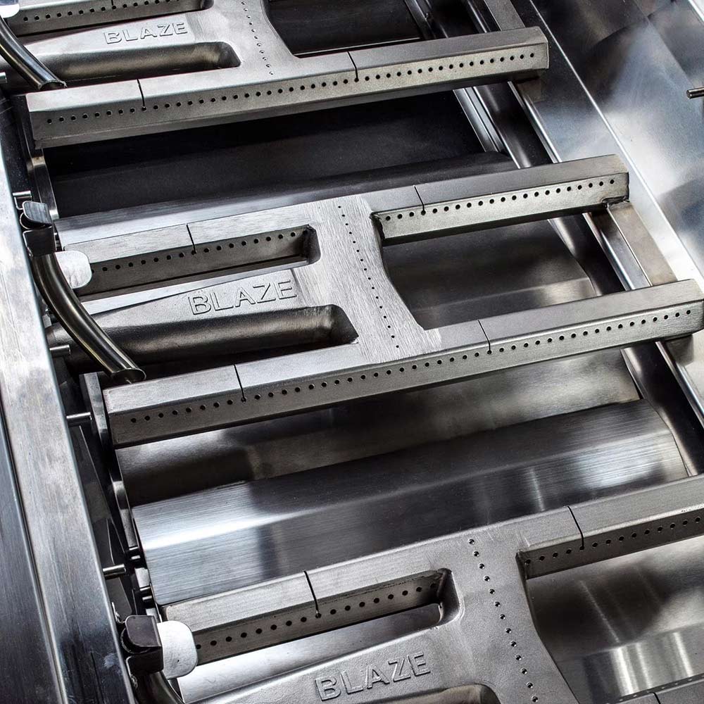 Stainless grill burner and heat plates with “BLAZE” markings inside the firebox