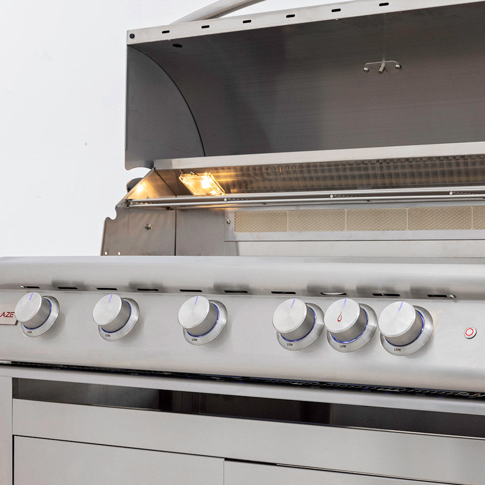 Gas grill burner tray with open hood, glowing flames under stainless hood.