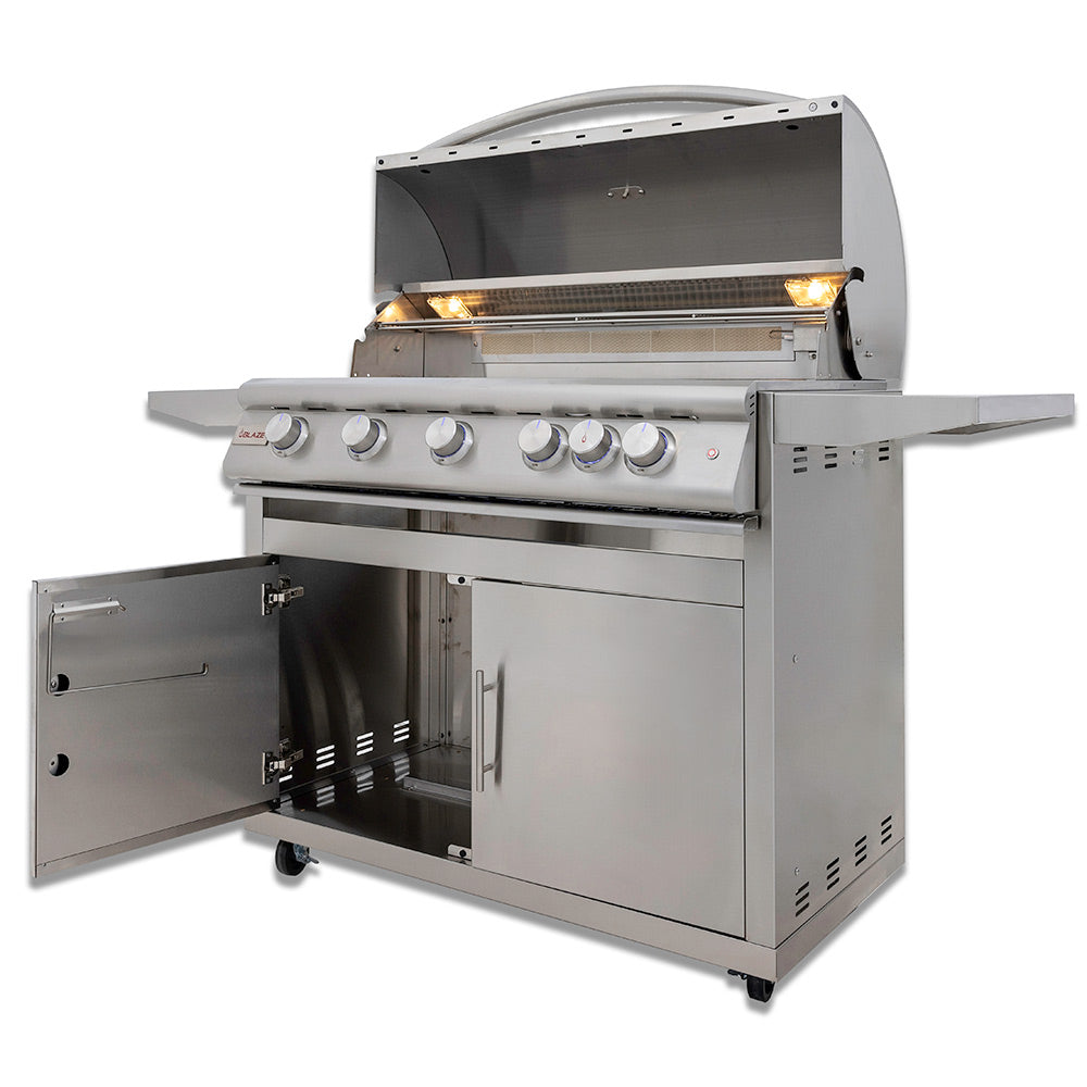 Gas grill on cart with side cabinet door open and hood lit over cooking grate.