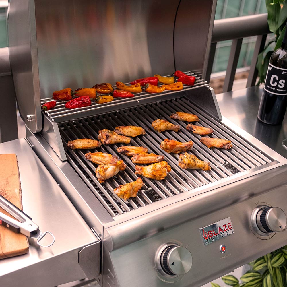 Stainless steel gas grill with open lid and cooking grates holding grilled meat