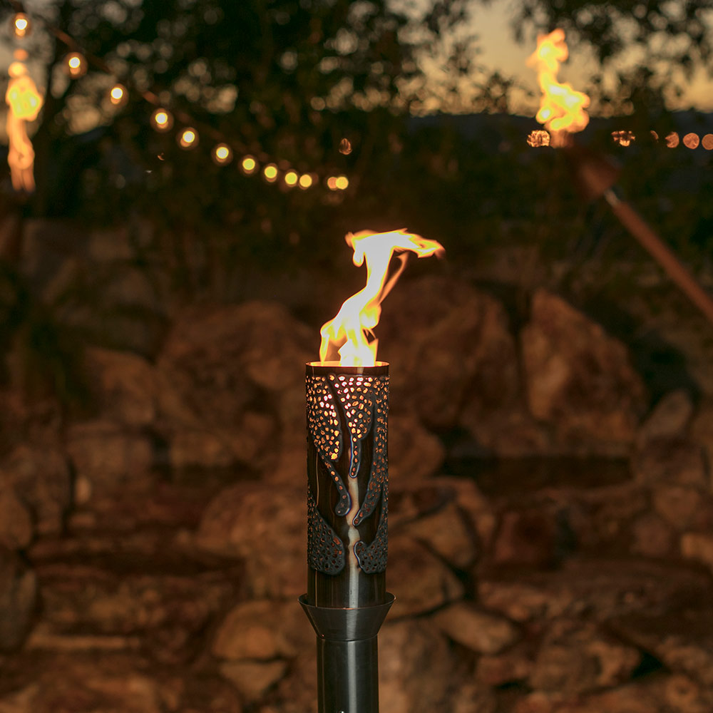 Lit gas torch head with flame rising from bird-patterned metal cylinder