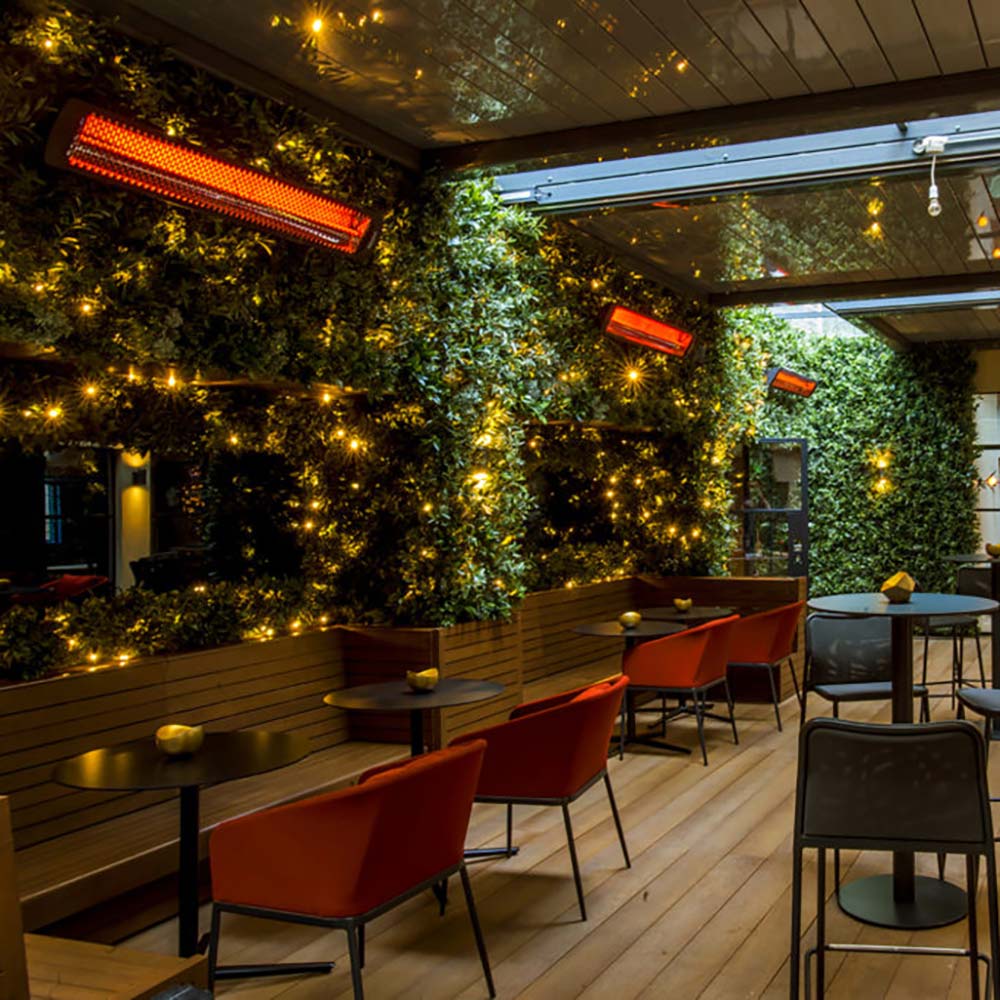 Outdoor patio heater with glowing orange infrared bar mounted under pergola