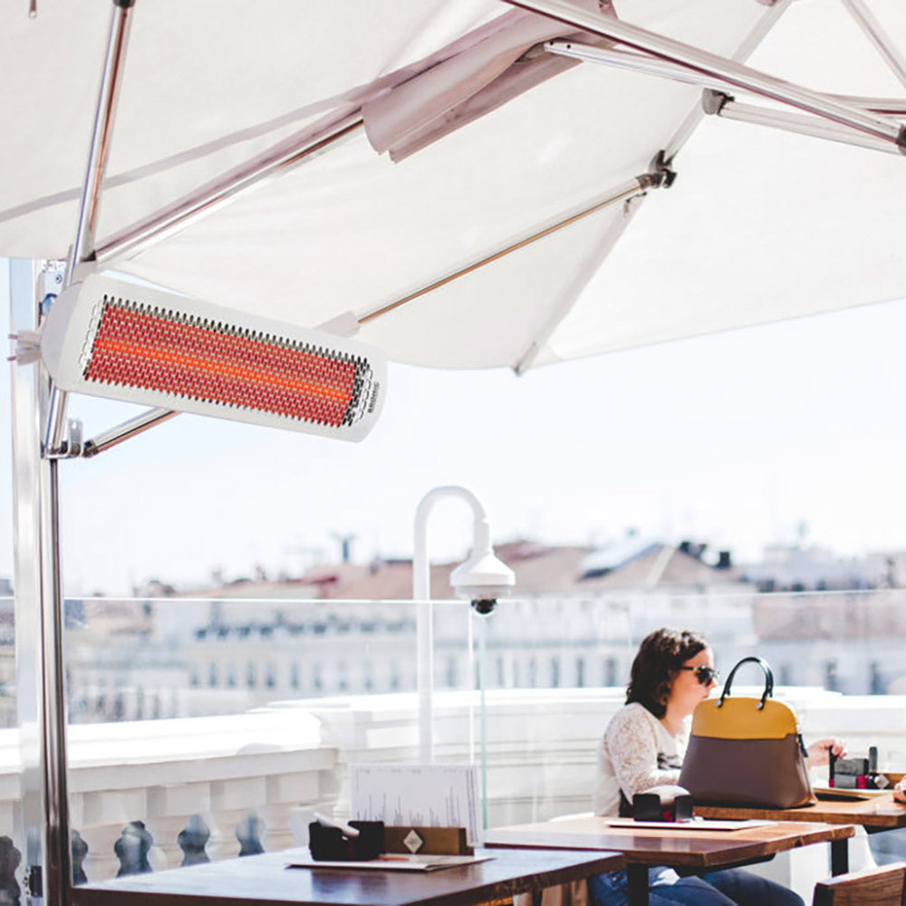 Electric heater with white housing and red heating element suspended under umbrella