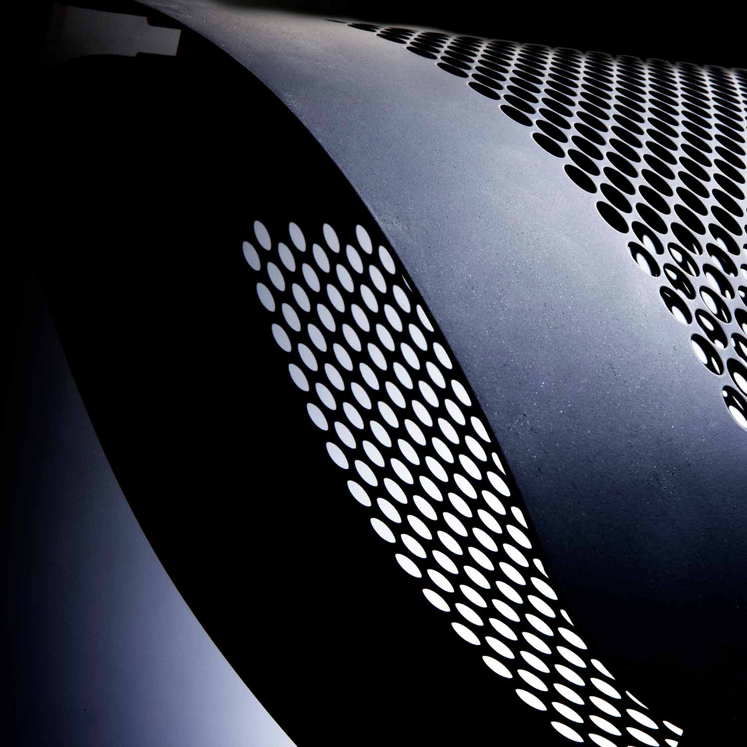 Heater vent grille with circular perforations on a dark metal body