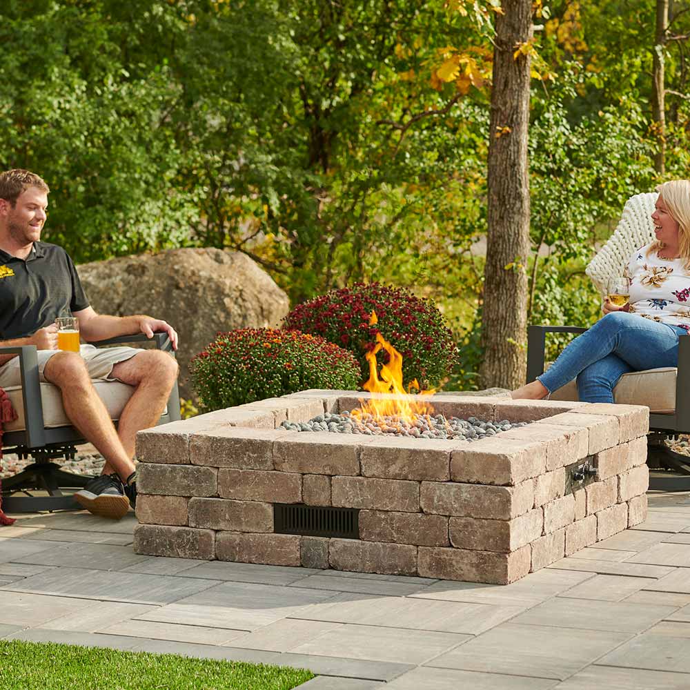 Outdoor square stone gas fire pit with flames and gray lava rocks