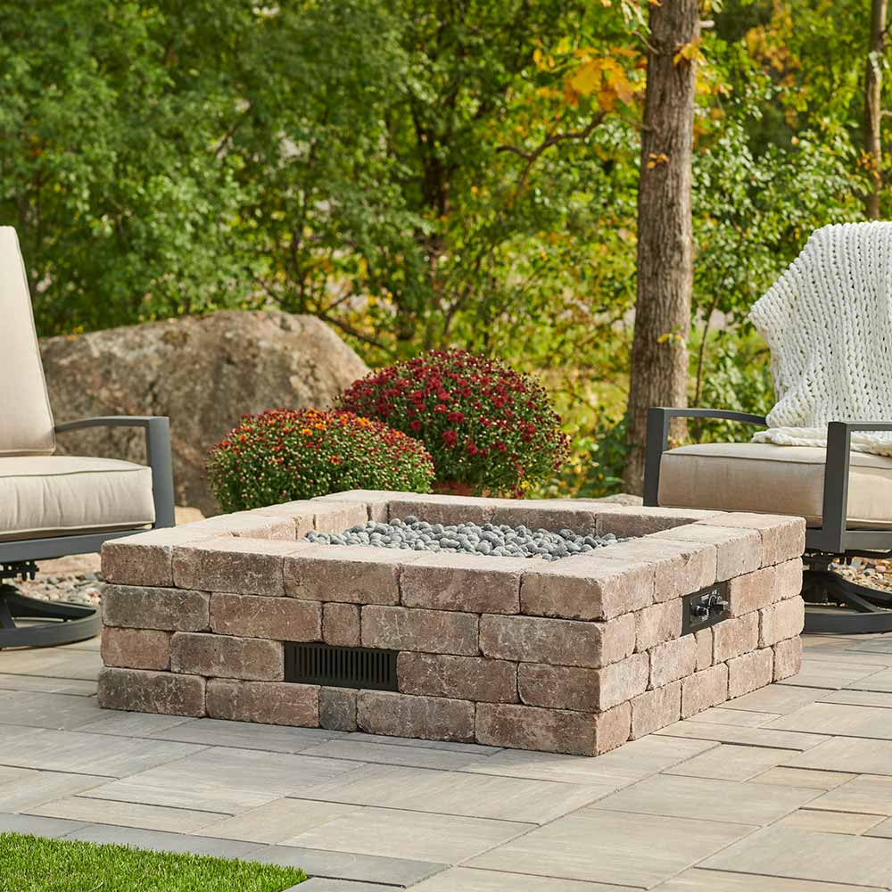 Outdoor square stone gas fire pit with gray lava rocks, flame not visible