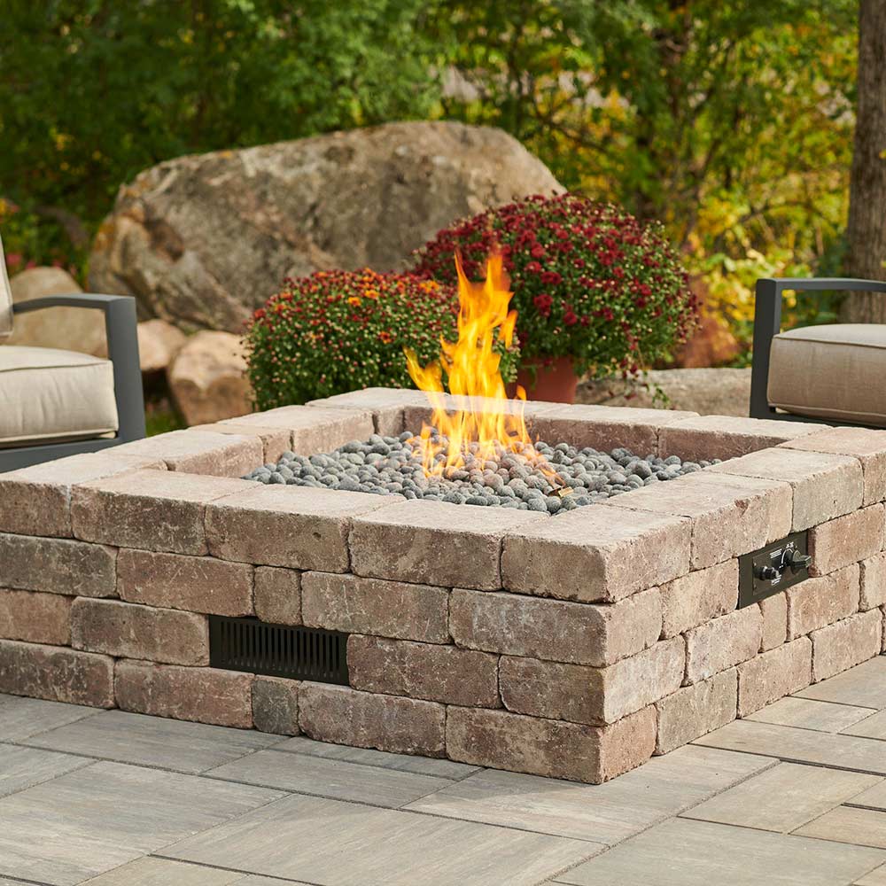 Square stone gas fire pit close-up with bright flames and gray lava rocks
